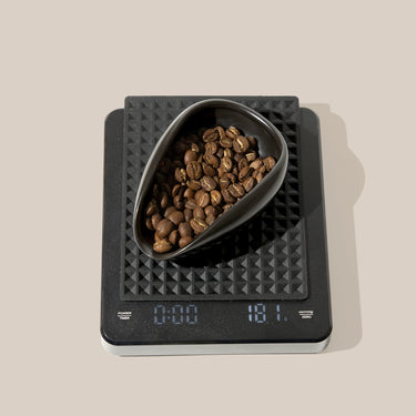 Digital kitchen scale with a bowl of coffee beans on a beige background