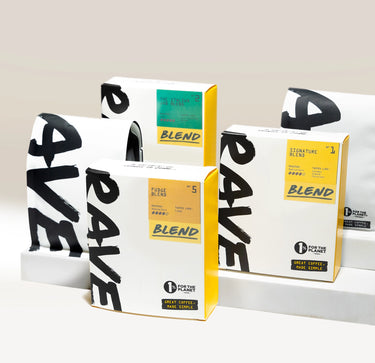 Four boxes of Ravecoffee’s Best Selling Blends – Whole Bean Variety Pack, featuring bold black lettering and vibrant labels, are displayed alongside two sleek white coffee bags on a light background. The modern packaging showcases the tagline “Great Coffee, Made Simple.” This popular Ravecoffee variety pack is ideal for anyone seeking convenient whole bean coffee with exceptional flavor.