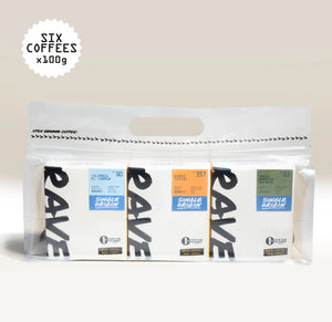 A clear bag displays six boxes of Ravecoffee’s Best Selling Single Origins - Whole Bean Variety Pack. Each box, with its own distinct colored label highlighting unique coffee details, offers a vibrant assortment of single-origin coffees. At the top left, text reads SIX COFFEES x 100g against a soft light gradient background.