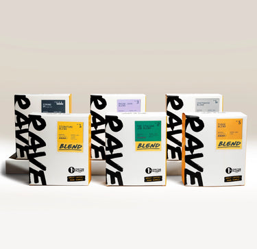 Discover the Best Selling Blends - Whole Bean Variety Pack by Ravecoffee: five boxes each showcasing a unique blend from Ravecoffee’s top collection. The variety pack features striking white packaging with bold black text and vibrant colored labels in yellow, green, blue, purple, and orange, arranged in two staggered rows—ideal for exploring a diverse selection of whole bean coffee flavors.