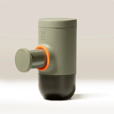 The WACACO Minipresso GR2, a compact cylindrical portable espresso maker in matte gray with an orange accent ring and plunger handle, stands upright on a neutral background.