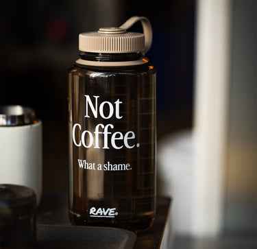 Brown water bottle with 'Not Coffee. What a shame.' text on a blurred background