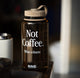 Brown water bottle with 'Not Coffee. What a shame.' text on a blurred background