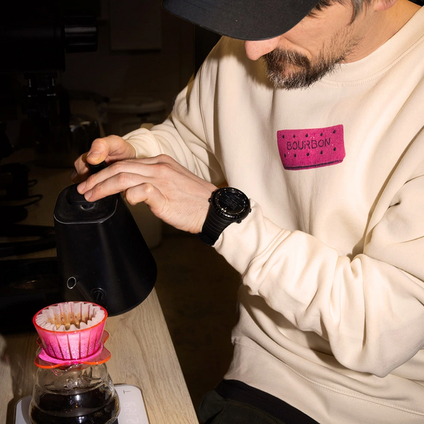 Person preparing coffee using a manual grinder and filter, wearing pink bourbon jumper.