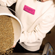Person holding a container of coffee beans with a 'Bourbon' label on a white jumper.